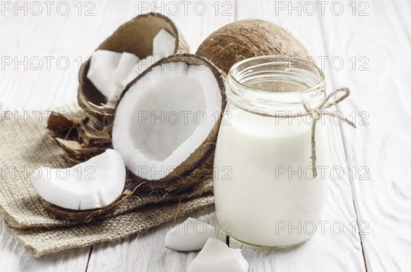 Mason jar of milk or yogurt on hemp napkin on white wooden table with coconut aside