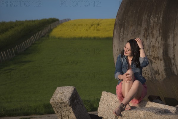 Attractive girl, casual dressed, with bare feet, eyes closed and smiling, sitting on a rock, in nature, enjoying the sunset, in South Moravia region