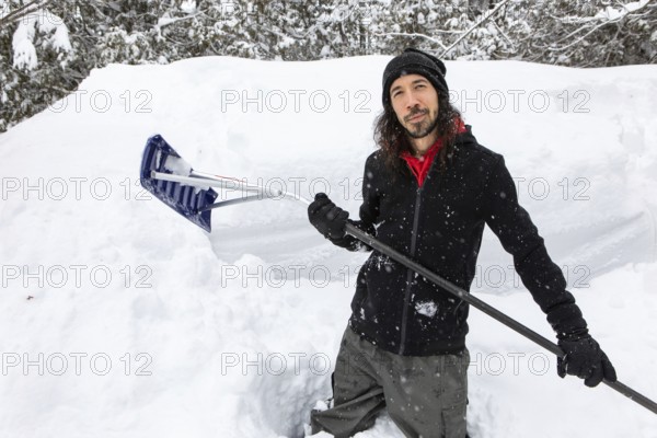 Satisfied and happy man smiling as he standing between snow piles holding a shovel to removing snows manually from the walkway after a heavy snowfall