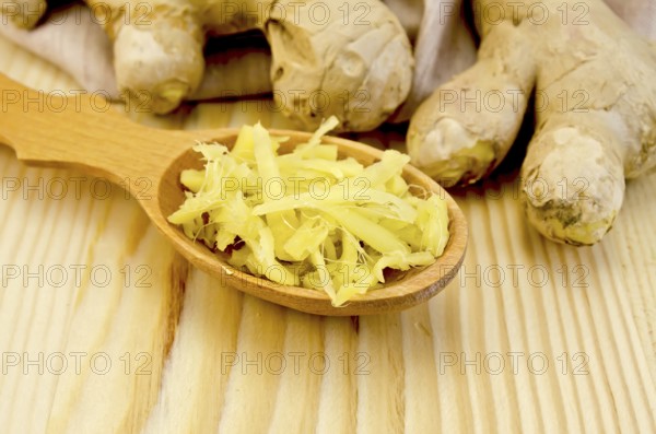 Wooden spoon with grated ginger, ginger root on a napkin on the background of wooden board