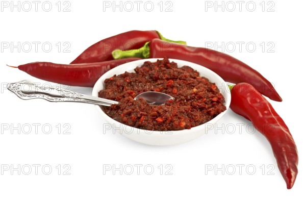 Tabasco in a white cup with spoon, fresh red peppers isolated on white background