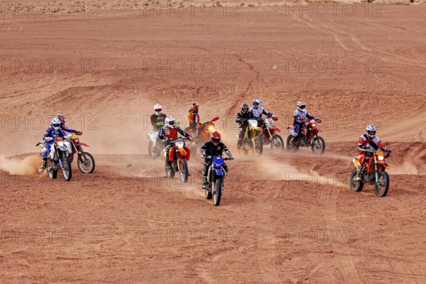 Several motorcyclists on the move, stirring up sand while driving in the desert, By off road vehicle through the Sahara desert in Algeria