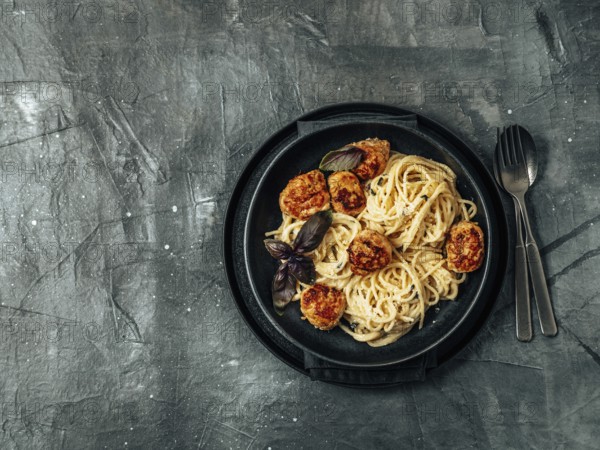 Zucchini Parmesan Meatballs with Pasta Carbonara in black craft plate over gray background. Close up view of creamy carbonara with copy space left. Top view or flat lay