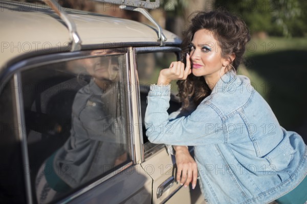 Funny young woman in a denim jacket with light-coloured make-up on the background of an old car