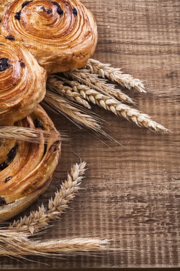 Ripe wheat ears rich rolls with raisins on oaken wooden board food and drink concept