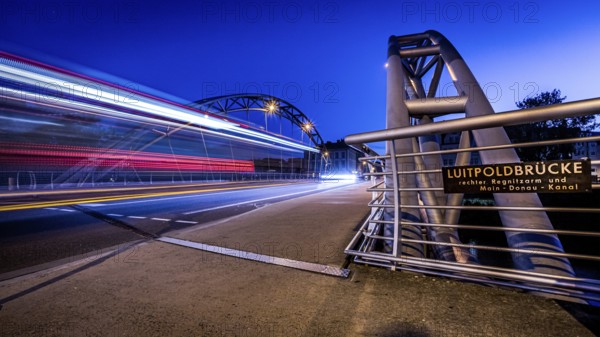 Night scene of an illuminated bridge with passing cars and an information sign, Luitpoldbrücke Bamberg