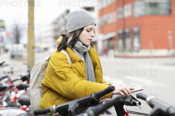 Woman in yellow jacket and cap on rental bikes in city street, cold winter day, environmentally friendly