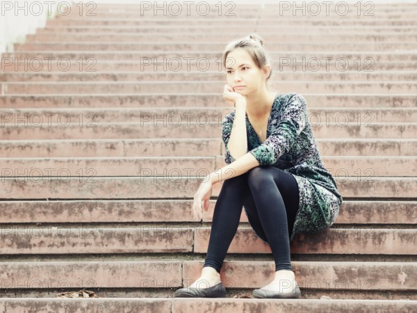 Sad lonely young woman sitting on steps. Portrait of serious girl with facial expression outdoors