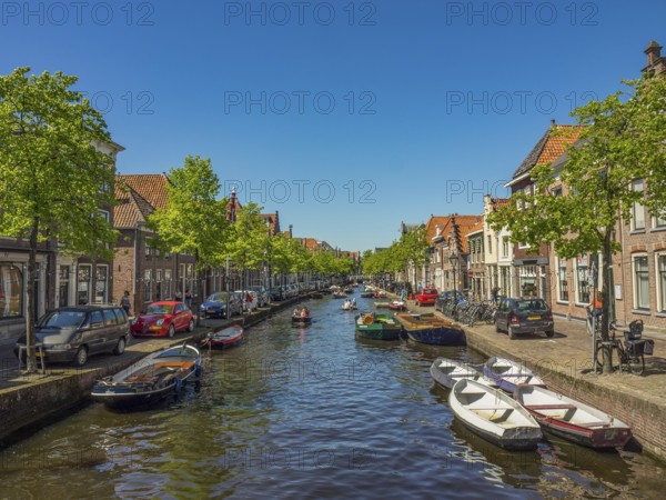 A long canal lined with boats, cars and historic buildings on a sunny day, alkmaar, the netherlands