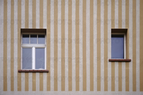 A house wall with a yellow and beige striped wall painting with two windows