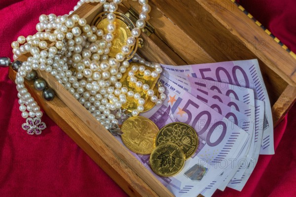 Gold in coins and bars with jewellery on red velvet. Symbolic photo for wealth, luxury, wealth tax. Austria