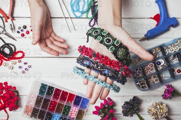 Plastic berries, flowers, beads and instruments for doing handmade headbands. Top view with hands