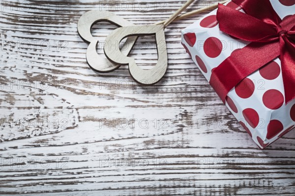 Present box with tied red bow wood hearts on vintage wooden board holidays concept