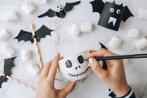 Female hands paint on white cup scary jacks face DIY for kids Halloween home activities Holiday art children craft Handmade decorations. Step by step Socially distanced at home Idea for art class