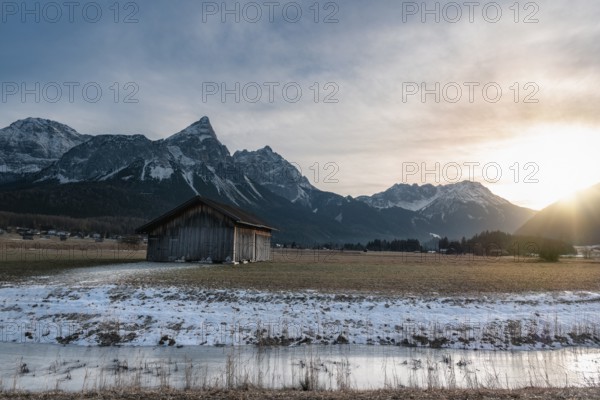 Winter alpine landscape with a wooden cabin, a frozen river and the snowy Alps mountains at sunset, near Ehrwald, Austria, Europe