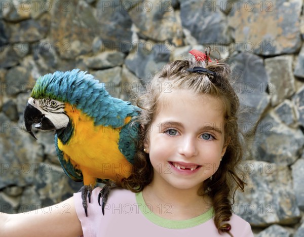 Blue eyes child girl with yellow parrot in her shoulder