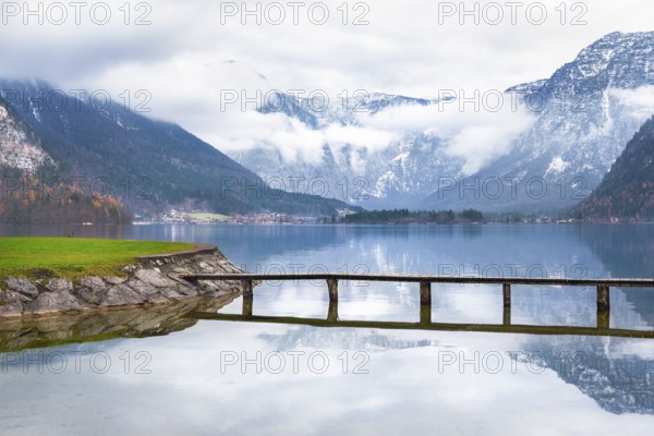 Trip idea theme image with the Hallstatter lake, a small bridge that crosses it and the majestic Northern Limestone Alps, located in Hallstatt town, Austria, Europe