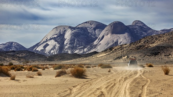 A vehicle moves along a dusty track through a vast desert landscape, travelling through the Sahara in Algeria by off-road vehicle