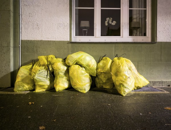 Photo of several bulging yellow rubbish bags that have been put out for collection at the roadside in front of a residential building. The yellow bags are part of the German recycling system and are used for plastic, metal and composite packaging materials, Düsseldorf, Germany, Europe