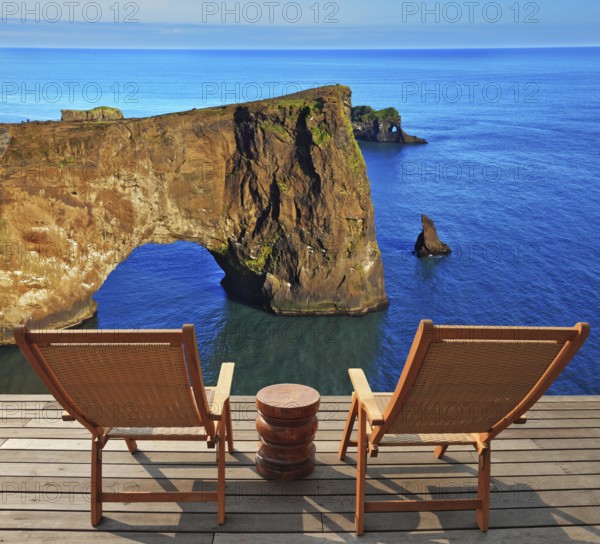 Cape Dirholaey in southern Iceland in July. The colossal rock lit summer sunset. On a coastal rock delivered comfortable wooden loungers