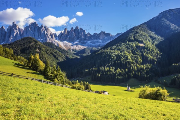 Little picturesque church of Santa Maddalena in Val di Funes. Sunny autumn day in Dolomites, Tirol. Rocky peaks and forested mountains surrounded by green Alpine meadows