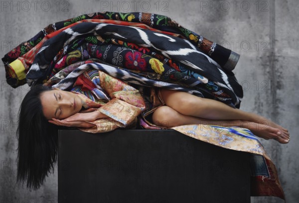 Sleeping beautiful woman lying on a black cube and covered by colorful blankets