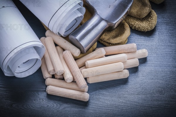 Close up view rolled blueprints hammer gloves wooden dowels
