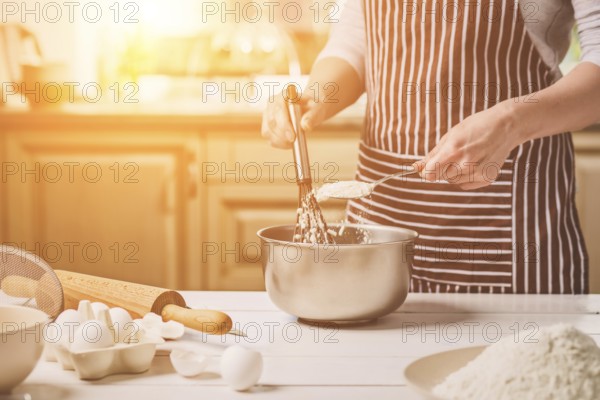 Young woman holding bowl with dough and whisk, closeup. A woman in a striped apron is cooking in the kitchen