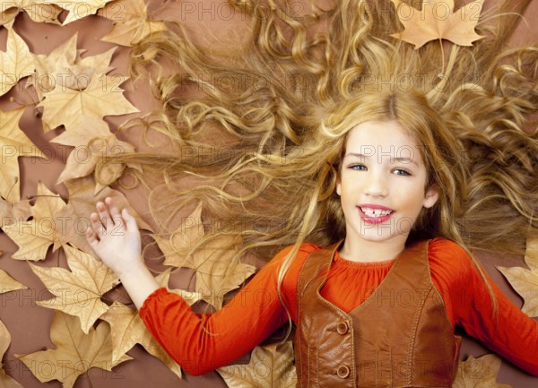 Autumn fall little blond girl on dried tree leaves background and long spread hair
