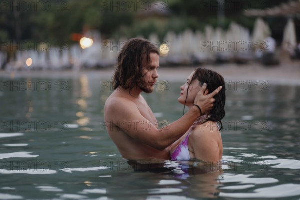 An intimate embrace between a couple in the ocean near the beach during the evening