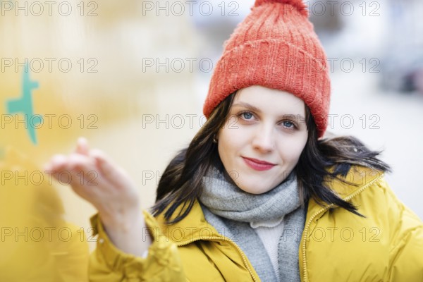 Woman with red hat and yellow jacket points with hand to large electric car for transport, electric mobility, environmentally friendly
