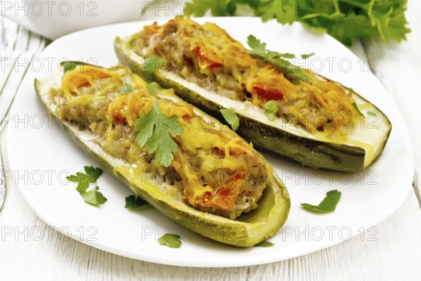 Cucumbers stuffed with minced meat, tomatoes, pepper with cheese and parsley in a plate, cream and greens sauce in a gravy boat, towel on the background of light wooden board