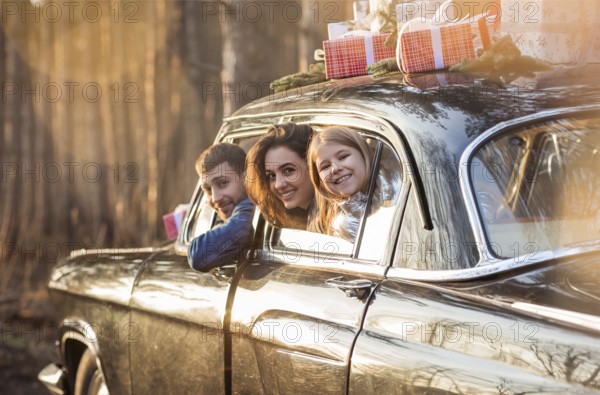 Overjoyed mother, father and little daughter looking out from window of car with Christmas presents on roof