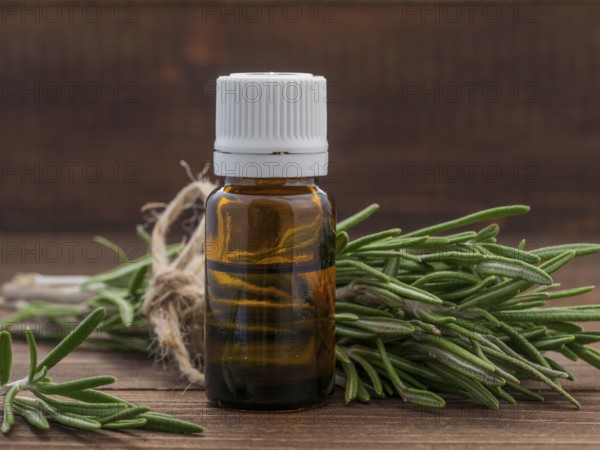 Rosemary essential oil in dark glass bottle and fresh rosemary on dark wooden background with copy space