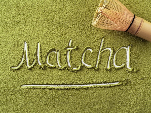 Matcha word over green matcha tea powder background and bamboo whisk Chasen. Top down view or flat lay