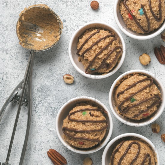Safe-to-eat raw monster cookie dough in small portion bowl, ice cream scoop and nuts on gray cement background. Ideas and recipes for kids and toddlers meal. Top view or flat-lay