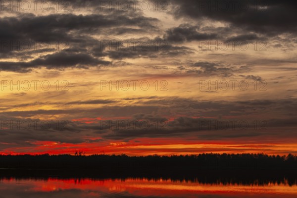 The stunning sunset showcases vibrant colors reflected on calm water, with dark silhouettes in the background