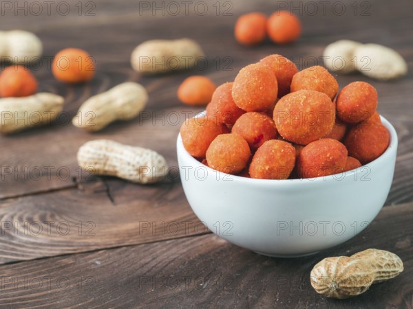 Peanut snack for beer, wine, party bar. Salted peanuts in red spicy chilli glaze on brown wooden table. Copy space