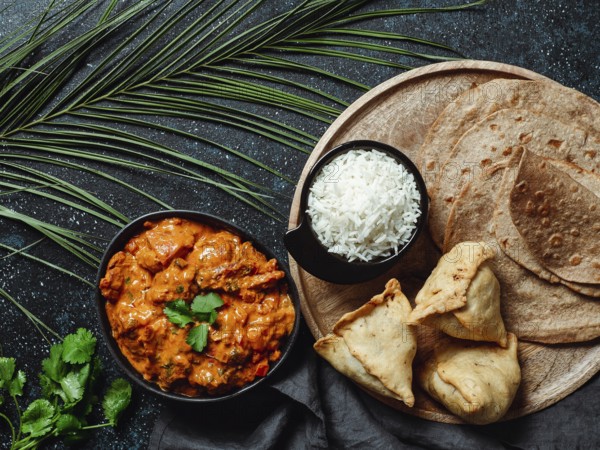 Indian cuisine dishes: tikka masala, rice, samosa, chapati, . Indian food on dark background with copy space. Assortment indian meal top view or flat lay