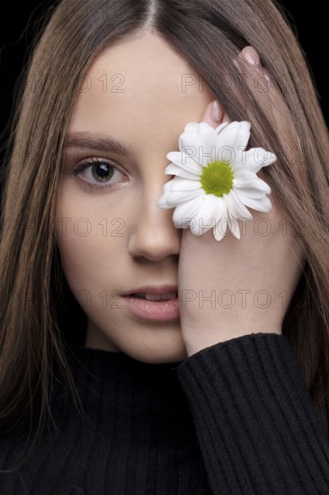 A beautiful girl with natural beauty holds a white flower near her eye. Young girl with a white chrysanthemum