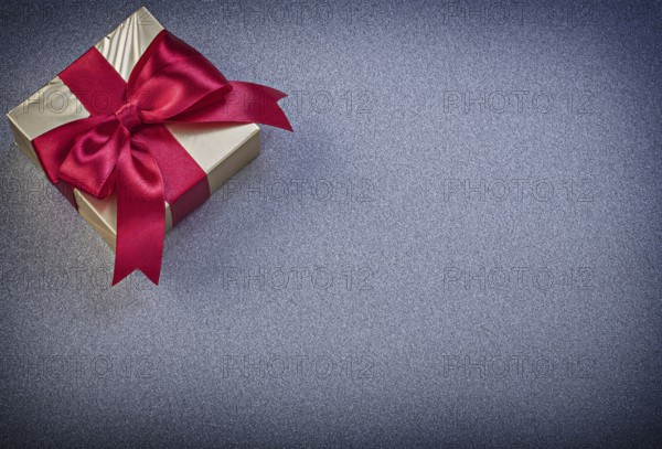 Present box with red knot on grey background holidays concept