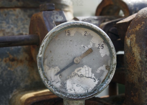 Old broken gauge with traces of numbers on the dial on a large old rusty engine