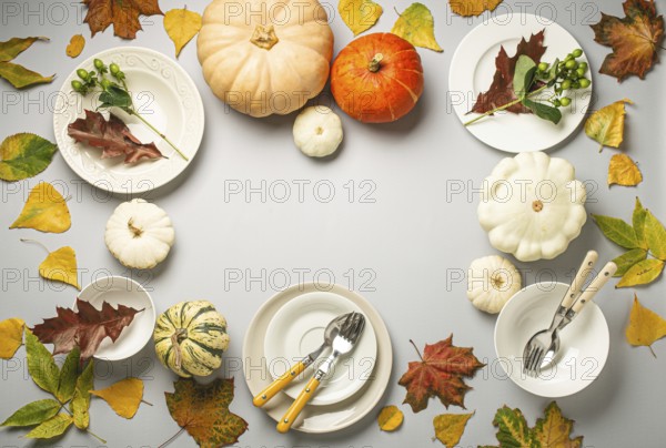 Thanksgiving festive table composition with different colourful pumpkins, autumn leaves, empty plates with cutlery on light grey background table ready for party and celebration. Space for text, food photography, food photography