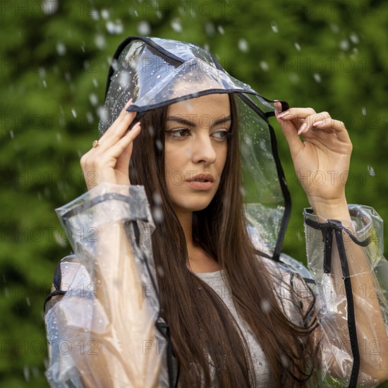 Young beautiful woman in hooded raincoat on rainy day