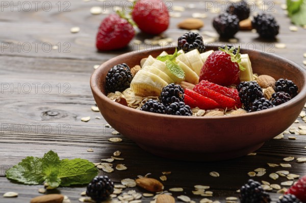 Fruit healthy muesli with banana strawberry almonds and blackberry in clay dish on wooden kitchen table
