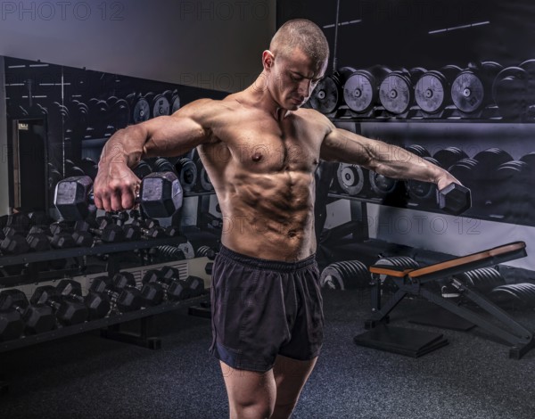 Young handsome sportsman lifting dumbbells in a gym