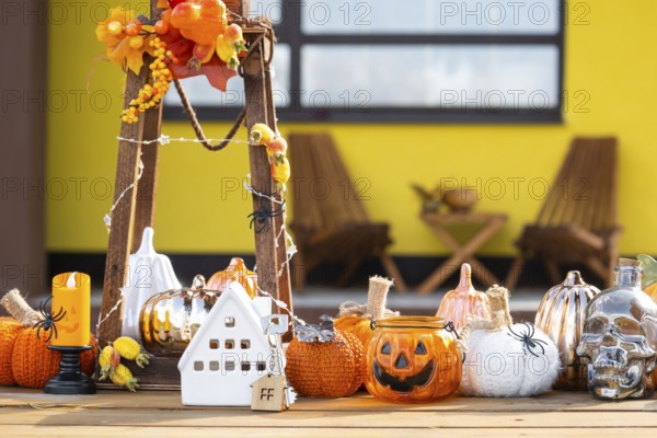 Autumn decor on porch of yellow house outside of pumpkin, lantern, garlands and figure of home and key. Halloween party, autumn mood, Harvest festival, real estate, insurance, mortgage