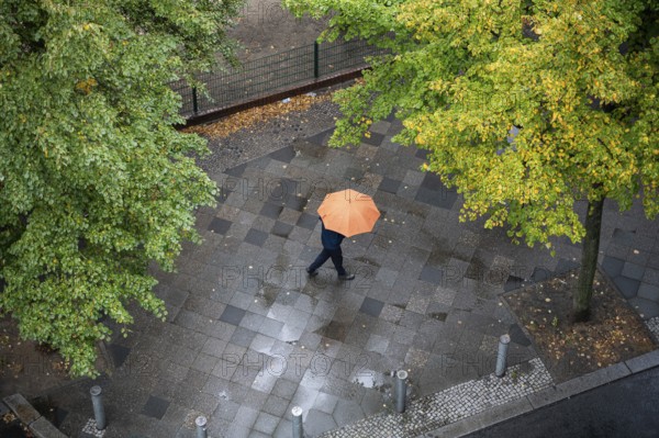 05.10.2023, Berlin, Germany, Europe, A person with an umbrella walks along a wet street in the Charlottenburg district of Berlin on a rainy autumn day, Europe