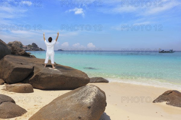 Middle-aged woman dressed in white doing yoga. Asana Blessing of the Sun. Thailand. Gorgeous beach on the Similan Islands