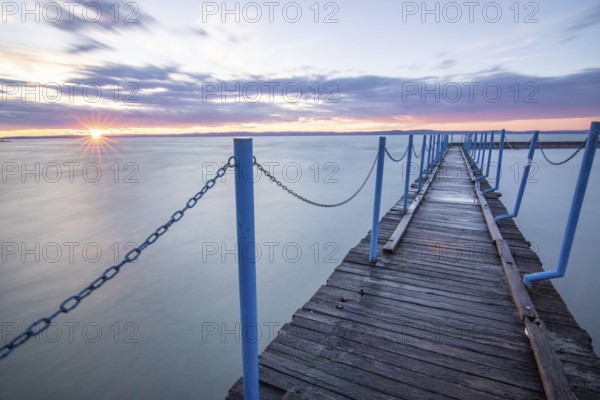 Water landscape, taken from the shore of a calm lake. View over the reflecting water to the horizon at sunset. a jetty or pier in the harbour of Siófok, Balaton, Hungary, Europe